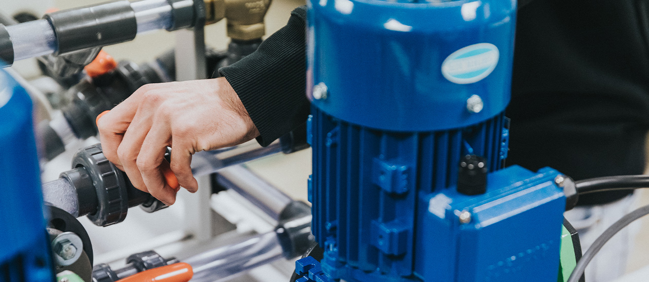 Een student uit de opleiding HVAC-systemen is met zijn handen bezig aan de leidingen van een technische installatie tijdens zijn opleiding op HOGENT campus Schoonmeersen.
