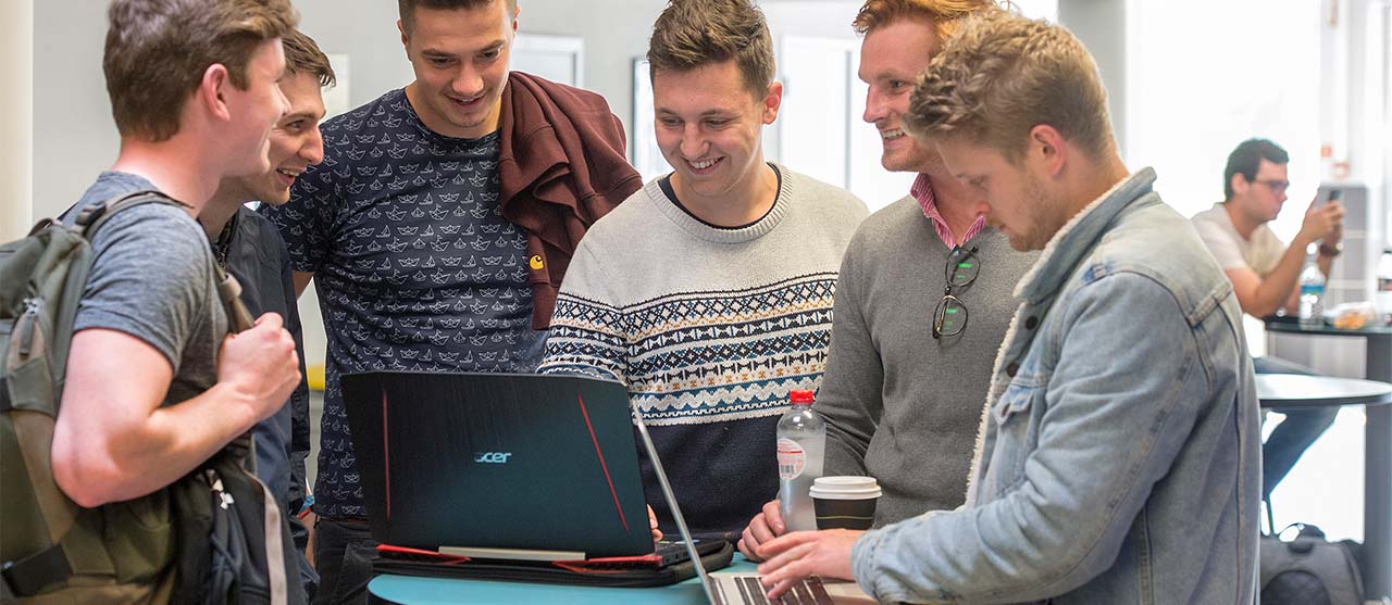 Lachende studenten toegepaste informatica van HOGENT experimenteren samen op hun laptops in het IT-lab.