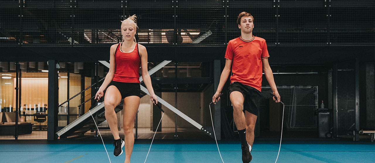 Twee studenten LO en bewegingsrecreatie van HOGENT tijdens een les ropeskipping in de sporthal.