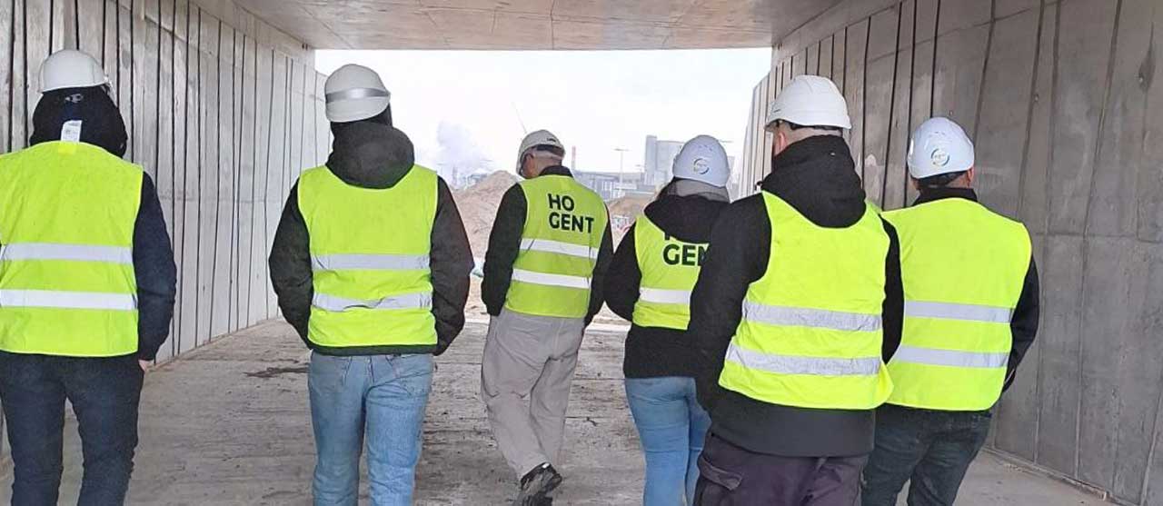 Studenten uit de graduaatsopleiding werforganisatie afstudeerrichting wegenbouw aan HOGENT wandelen uitgerust met fluohesjes en veiligheidshelmen door een tunnel op werfbezoek bij de werken aan de R4 West & Oost.