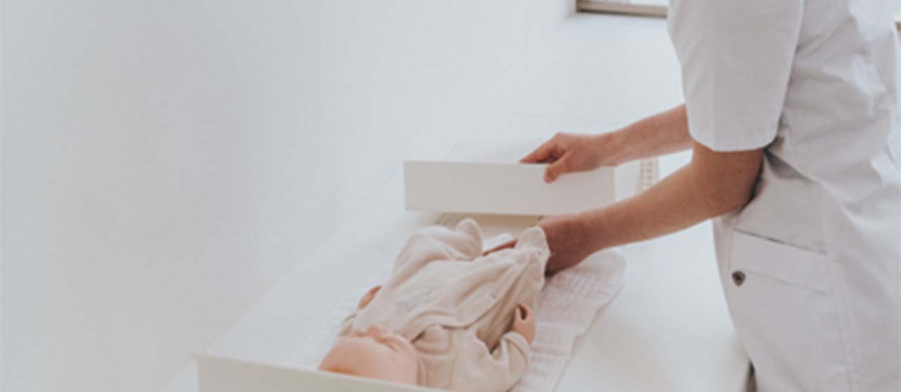 Een studente uit de graduaatsopleiding basisverpleegkunde van HOGENT legt een baby op een zorgbed.