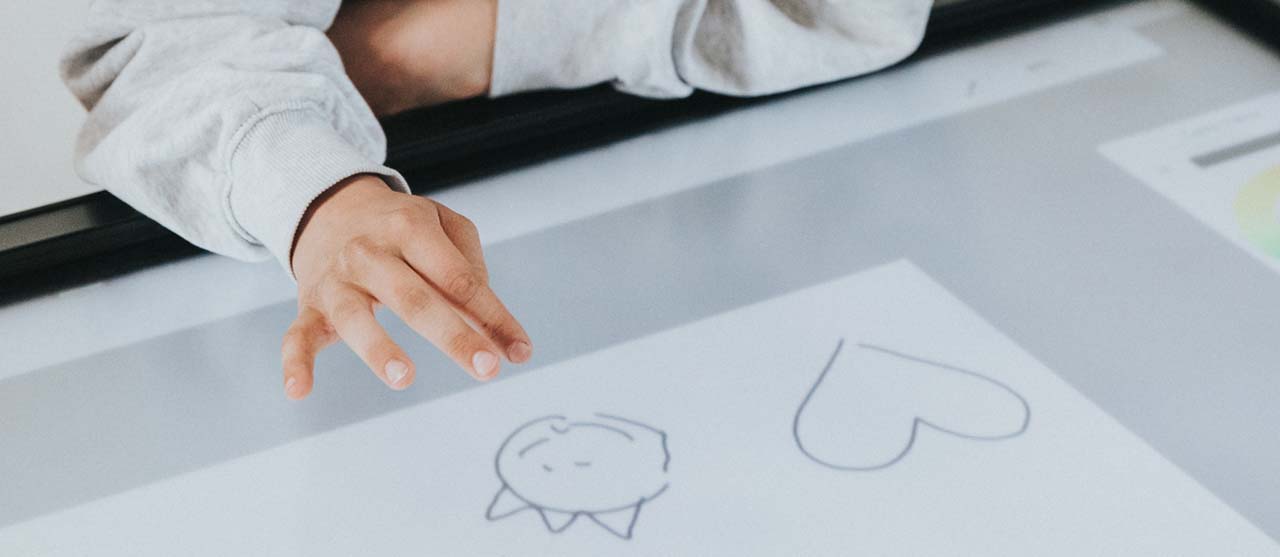 Een meisje tekent een dino en hartje op een lichtbak tijdens de stageles van een student lager onderwijs van HOGENT.