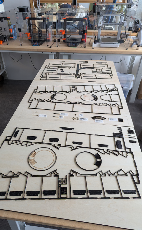 Maquette van gebouw T in het BIBLAB met het grondplan van de 3 verdiepingen in 3D geprint en bevestigd op houten platen. Op de achtergrond staan de 3D-printers.