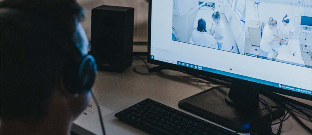 Een student uit de bachelor medische technologie van HOGENT observeert studenten verpleegkunde in het zorglab.