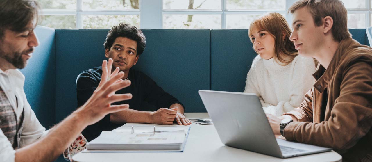Studenten secundair onderwijs luisteren naar een enthousiaste lector in een zetelhoek in de gang van campus Ledeganck.