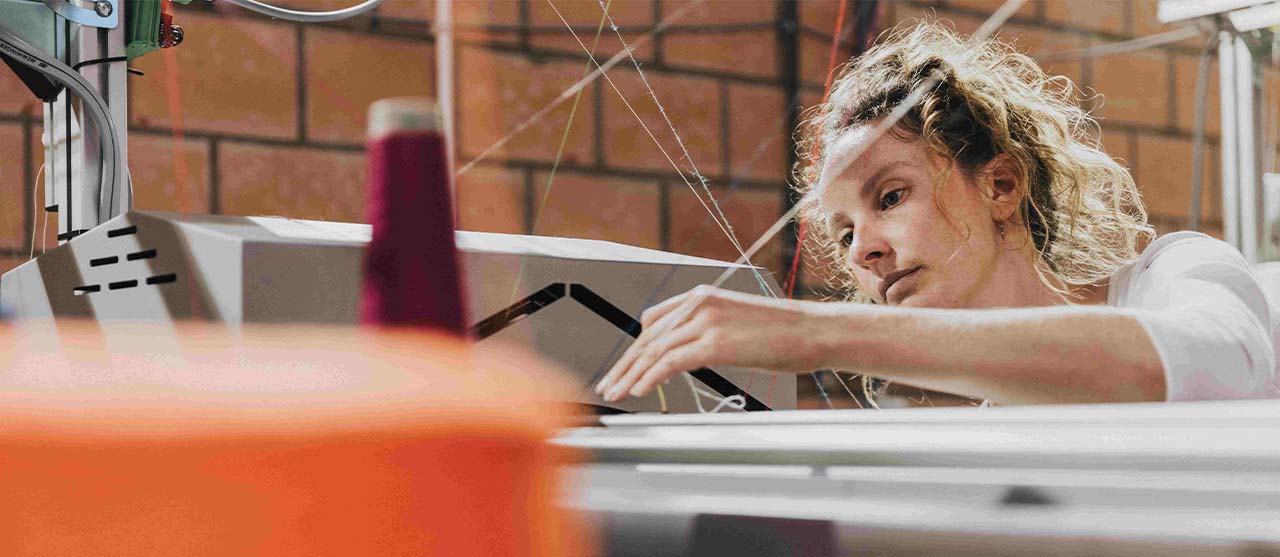 Studente textieltechnologie van HOGENT bedraadt een industriële breimachine.