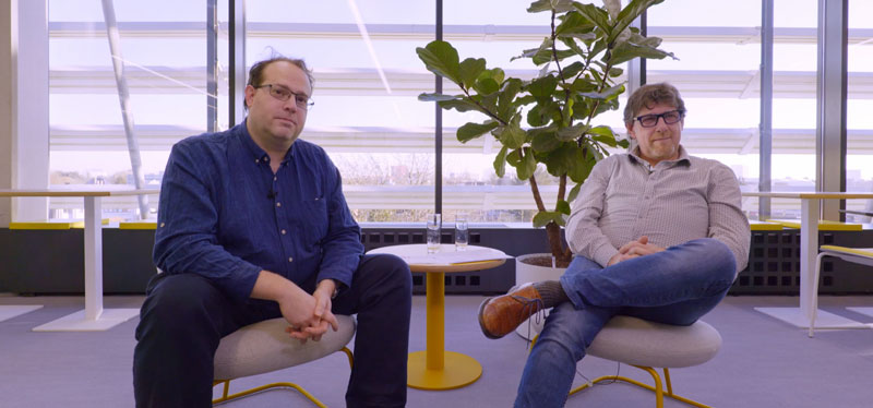 Screenshot video met twee mannen in stoel tijdens interview
