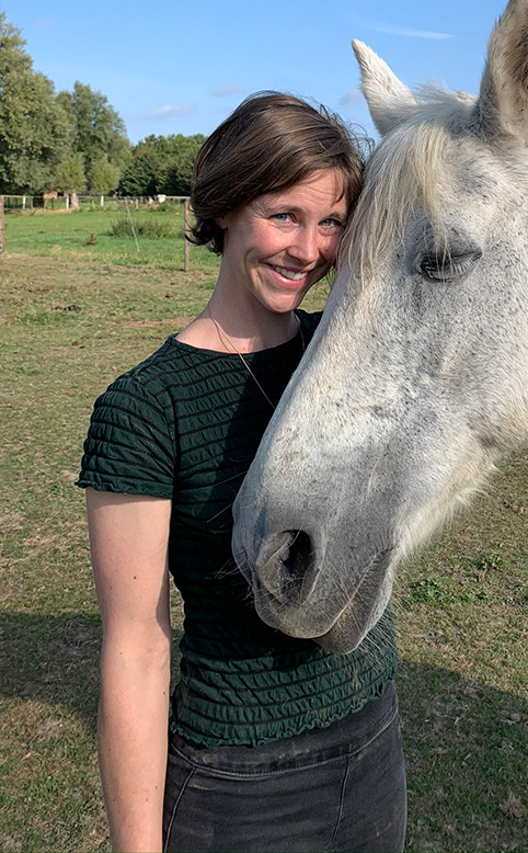 Anaïs Dupont, oud-studente uit de bachelor ergotherapie van HOGENT poseert naast een paard bij haar praktijk 'Hoefspoor'.